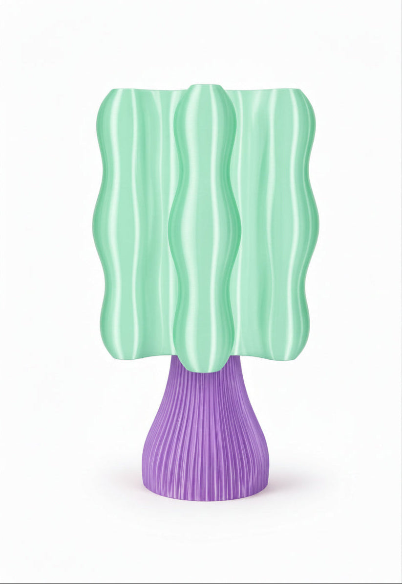 A modern sculptural table lamp with a wavy mint green shade and a ribbed purple base, shown against a plain white background.