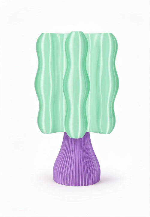 A modern sculptural table lamp with a wavy mint green shade and a ribbed purple base, shown against a plain white background.